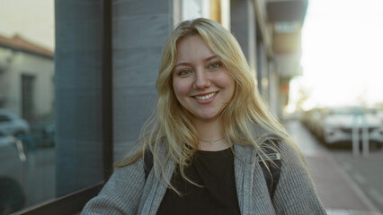 Young woman smiling outside on city street with blonde hair wearing casual clothes under sunlight...