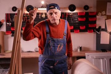Aggressive mature carpenter showing fist to camera with negative emotions, working on furniture renovation. Handmade, small business, DIY and entrepreneurship