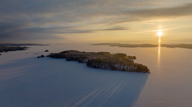 Aerial view of the serene, snow-covered landscape, reflecting the golden sunset, a peaceful winter scene, North Karelia, Finland.