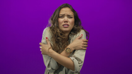Woman shivering against a vivid purple background, expressing cold discomfort with arms crossed...