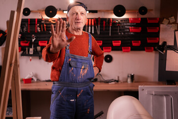 Mature carpenter showing stop gesture, rejecting job proposal for furniture renovation in workshop. Handmade, small business, DIY and entrepreneurship