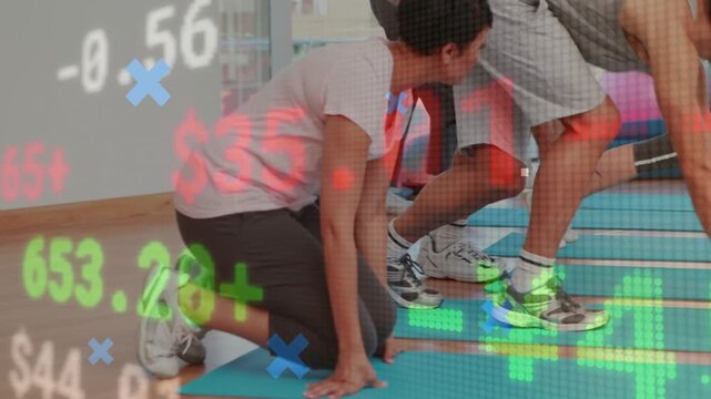 Class following cue, lowering onto mats into quadruped while finance charts overlaying group