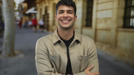Fototapeta premium Man places arms forward, crosses them firmly, then stands on street corner, guy showing young hispanic urban smiling confidence.