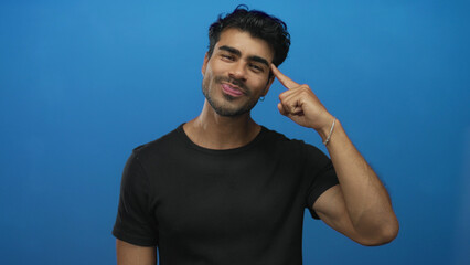 Man wearing black tshirt with finger pointing to head standing in studio with blue backdrop and...