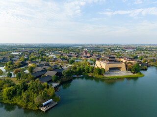Obraz premium Xiantao city landscapes show traditional Chinese architecture along water surrounded by green trees under a cloudy sky.