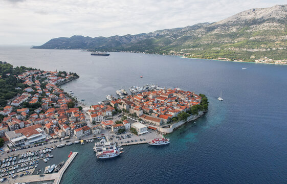 Aerial view of terracotta roofs and stone buildings create a tapestry against the azure sea, cradled by majestic mountains, Korcula, Dubrovnik-Neretva County, Croatia.