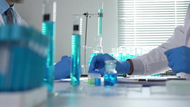 Two scientists in a laboratory collaborating on an experiment. They are handling beakers and vials with blue liquid and taking notes