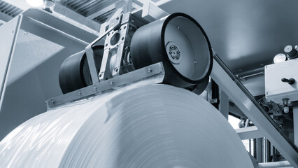 Automatic polyethylene plastic bag production machine with lighting effect. Close-up of the roller of the plastic bag production machine in the light blue scene. product packaging concept