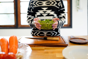 young female holding bowl of fresh salad standing in the home kitchen. Woman cooking healthy food, dinner or breakfast