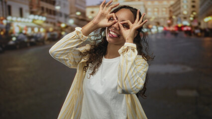 Fototapeta premium Woman making hand binoculars with fingers over eyes on a busy city street lit by evening bokeh lights; joyful curiosity.