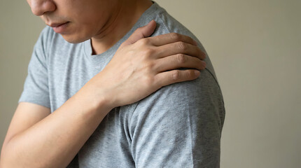 Person gripping their shoulder firmly with the opposite hand, upper body rotated slightly, head cropped at the nose downward, plain solid background