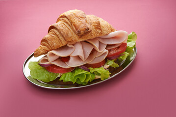 croissant with ham on silver tray on purple background