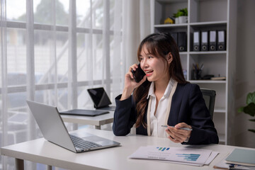 Asian businesswoman talking on phone and working with laptop in office