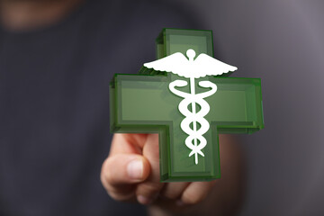 Hand interacting with a 3D medical cross with caduceus. Concept of healthcare, medicine, treatment, and wellbe