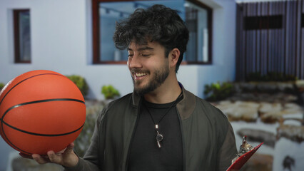 Young hispanic man outdoors holding basketball smiling under sunny sky