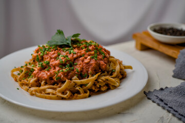 a plate of spaghetti topped with sauce and a small plate of black pepper are in the background.