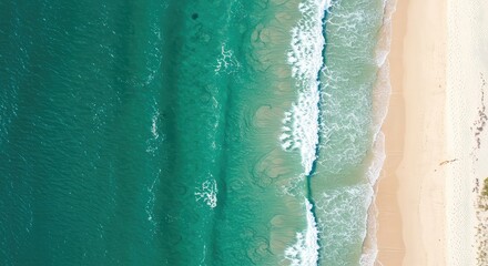 Aerial view of turquoise ocean waves gently lapping against pristine sandy beach shoreline on a sunny day with white foam