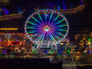 Aerial view of the Edinburgh Christmas Market's towering Ferris wheel ablaze with rainbow lights against the inky night sky, a spectacle of festive cheer, Edinburgh, Scotland, United Kingdom.
