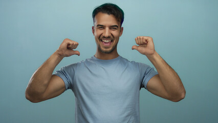 Fototapeta premium Hispanic man pointing at himself with thumbs over isolated blue background, expressing confidence and self-assurance in a casual setting.