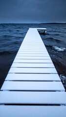 Obraz premium Snow covers the dock by the lake as waves crash under a gray sky at dusk
