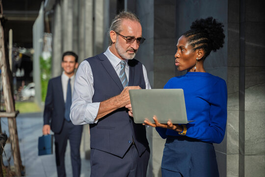 Group of diverse business professionals discussing a project outside an office building. The scene captures leadership, teamwork, strategic planning, and corporate communication in natural daylight. - Powered by Adobe