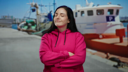 Obraz premium Woman in pink hoodie stands at a port with ships and boats in the background, expressing emotion.