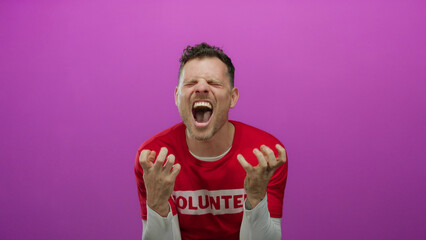 Hispanic man expressing emotion in volunteer t-shirt against vibrant pink background in isolated...