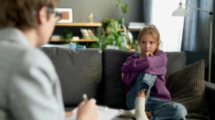 Thoughtful girl child listening to female therapist sitting on couch in counselling office during psychotherapy session, AI generated video