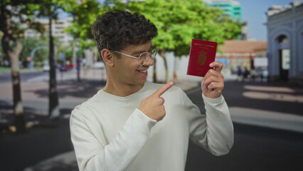 Man smiling and holding danish passport points finger at passport on street; travel excitement...