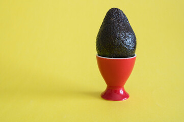 Avocado on an egg stand on yellow background. Vitamin and healthy Easter concept.