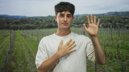 Obraz premium Man places hand on chest and raises right hand in a forest field, palm visible and direct gaze; sincere apology.