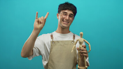 Man holding wooden mannequin and making rock horns gesture in turquoise studio; playful creativity...