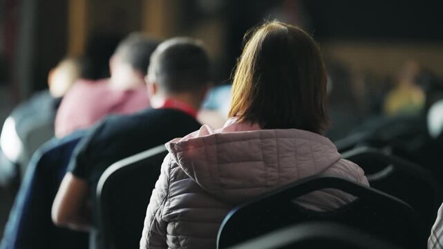 Unrecognizable business people are gathered in a dimly lit conference room, attentively listening to a presentation
