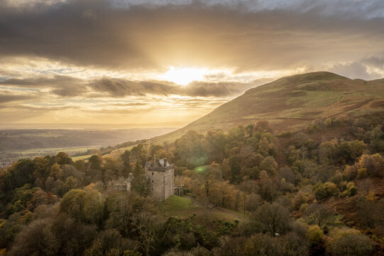 Aerial view of Castle Campbell nestled among the Ochil Hills, bathed in the warm glow of the setting sun, Dollar, Scotland, United Kingdom.