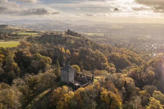 Aerial view of the stark stone ruin of Castle Campbell rises from a sea of autumnal trees under a golden sky, Dollar, Scotland, United Kingdom.