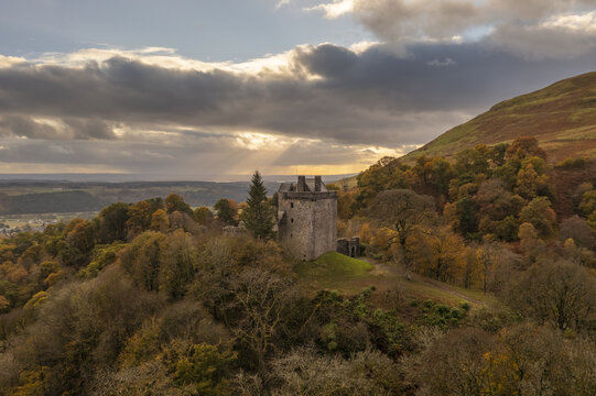 Aerial view of Castle Campbell amidst the vibrant autumn foliage under a dramatic sky, a solitary sentinel overlooking the serene Scottish landscape., Dollar, Scotland, United Kingdom.