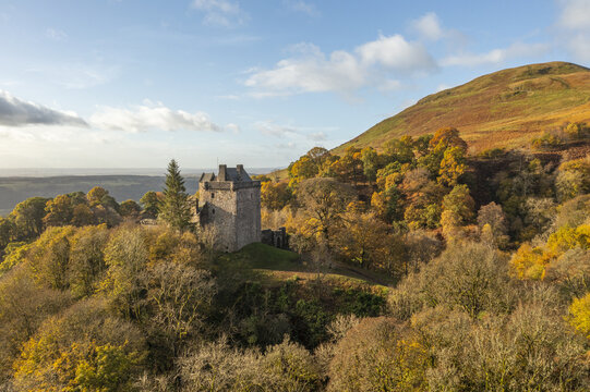 Aerial view of Castle Campbell stands in stark contrast to the vibrant autumn foliage and rolling hills under a serene sky, Dollar, Scotland, United Kingdom.