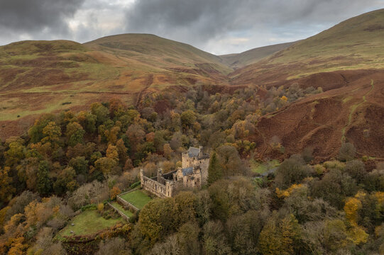 Aerial view of Castle Campbell nestled among the colorful autumn trees at the base of the Ochil Hills under a cloudy sky, Dollar, Scotland, United Kingdom.