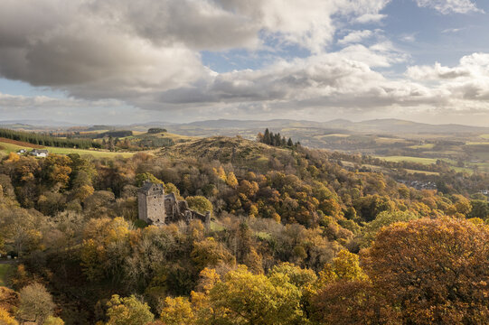 Aerial view of autumnal foliage blankets the rolling hills surrounding Castle Campbell, its ancient stone walls a stark contrast to the vibrant leaves, Dollar, Scotland, United Kingdom.