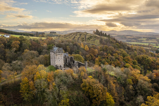 Aerial view of Castle Campbell standing proud amidst the vibrant autumn foliage, the sky painted with hues of gold and amber, Dollar, Scotland, United Kingdom.