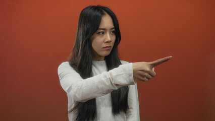 Woman pointing assertively forward against isolated red background implying urgency or direction with intense expression creating a commanding visual impact in the frame