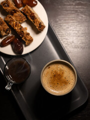 Top view of aromatic coffee cup served with crunchy nut biscuits and sweet dates on a gray tray