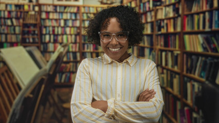 Woman wearing glasses with arms crossed smiling in a historic library with rows of bookshelves and a wooden bookstand  confidence. © Krakenimages.com