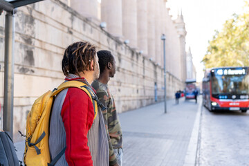 Two diverse men with dreadlocks and camouflage shirt waiting for a bus at a city stop