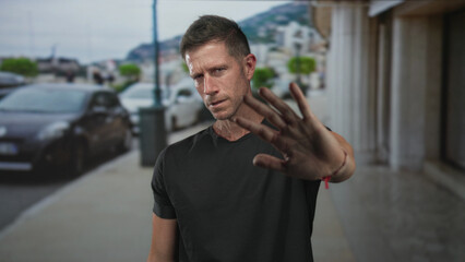 Man with hands raised palms out on street blocking forward movement, facing camera; caution pause...