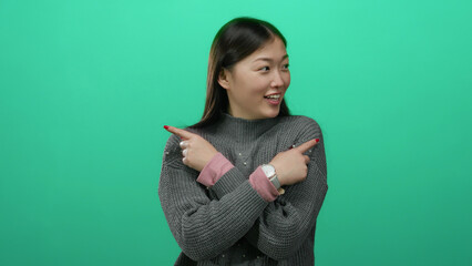 Obraz premium Woman smiling while pointing in opposite directions against vibrant green backdrop wearing cozy sweater and pink watch highlighting playful expression and modern style