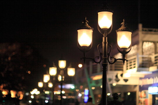 View of vintage streetlights casting a warm glow along a bustling avenue, illuminating the night with a soft, inviting light, Karachi, Sindh, Pakistan.