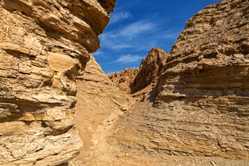 View of rugged, layered rock formations carve a narrow path under a bright blue sky, creating a striking contrast of textures and colors, Karachi, Sindh, Pakistan.