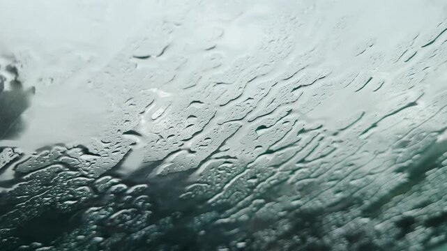 Raindrops are seen on a vehicle's windshield, creating an abstract water pattern