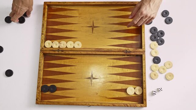 Top-down view of hands carefully setting up the pieces on a backgammon board. A player prepares for a strategic challenge, moving checkers to their starting positions before a fun game begins.